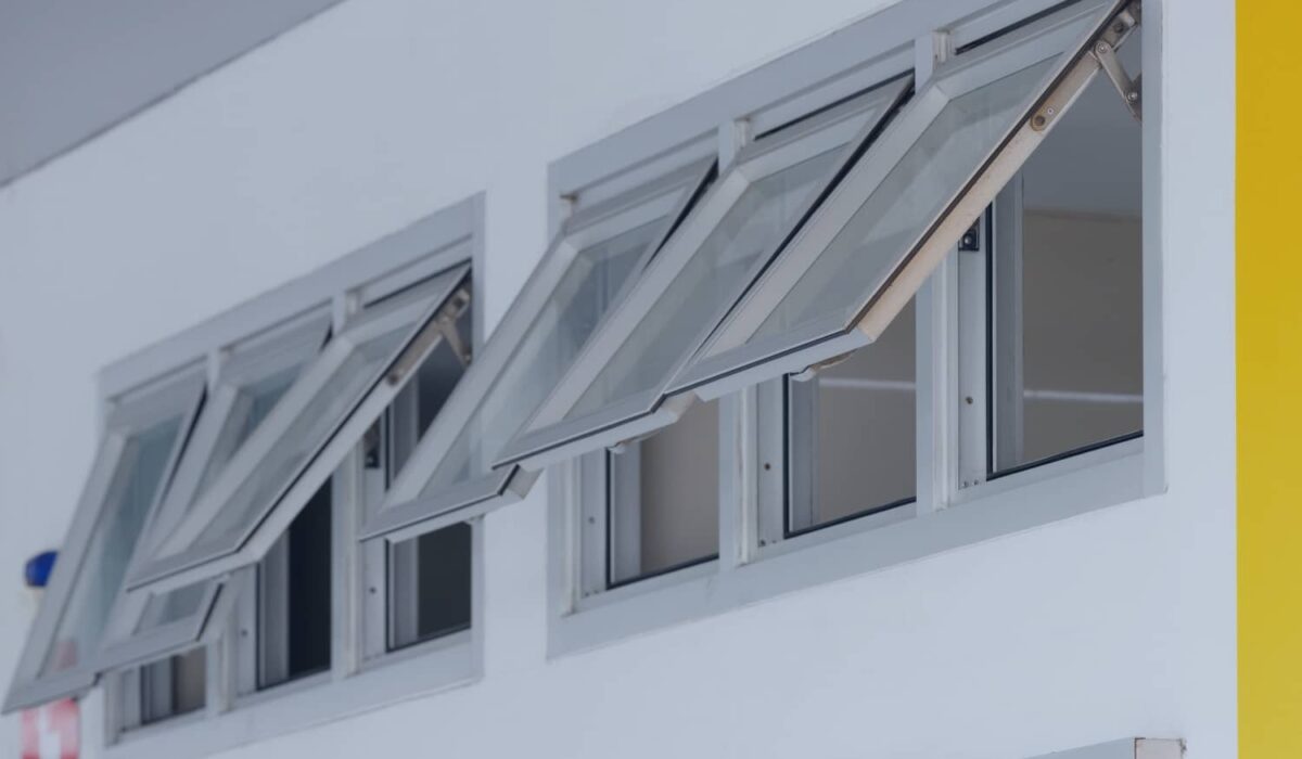 A row of modern silver-framed awning windows are hinged at the top and cranked open outward along a clean white wall.