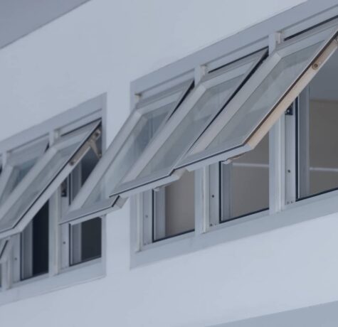 A row of modern silver-framed awning windows are hinged at the top and cranked open outward along a clean white wall.
