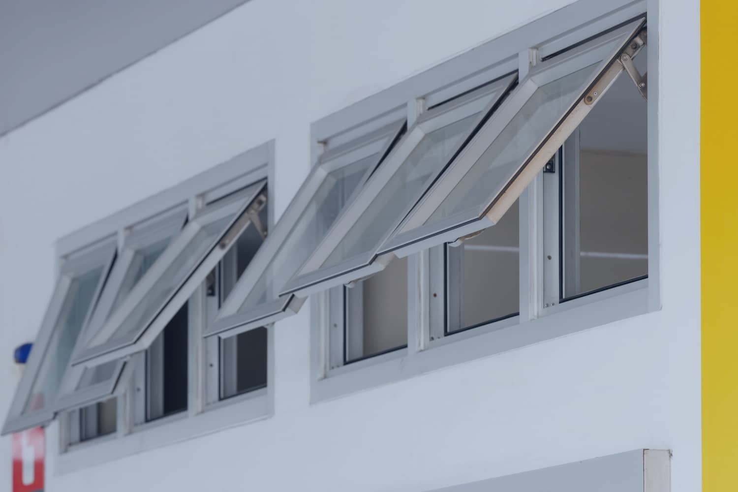 A row of modern silver-framed awning windows are hinged at the top and cranked open outward along a clean white wall.