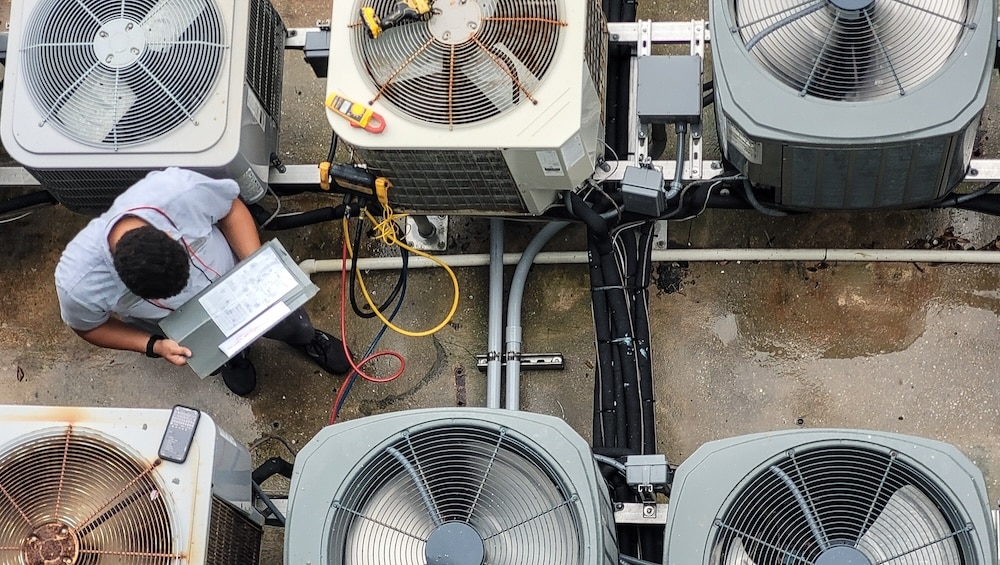 An overhead view of an inspector using diagnostic tools and a clipboard to evaluate multiple commercial rooftop HVAC units.
